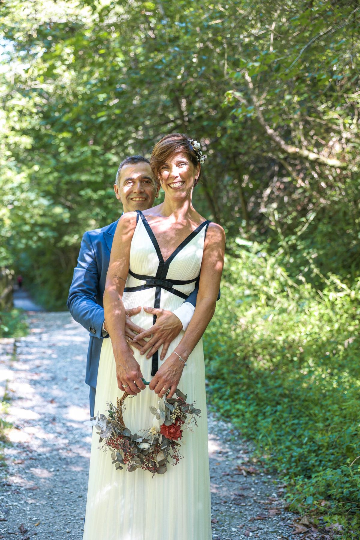 Novios abrazados y sonriendo a cámara en un camino del bosque