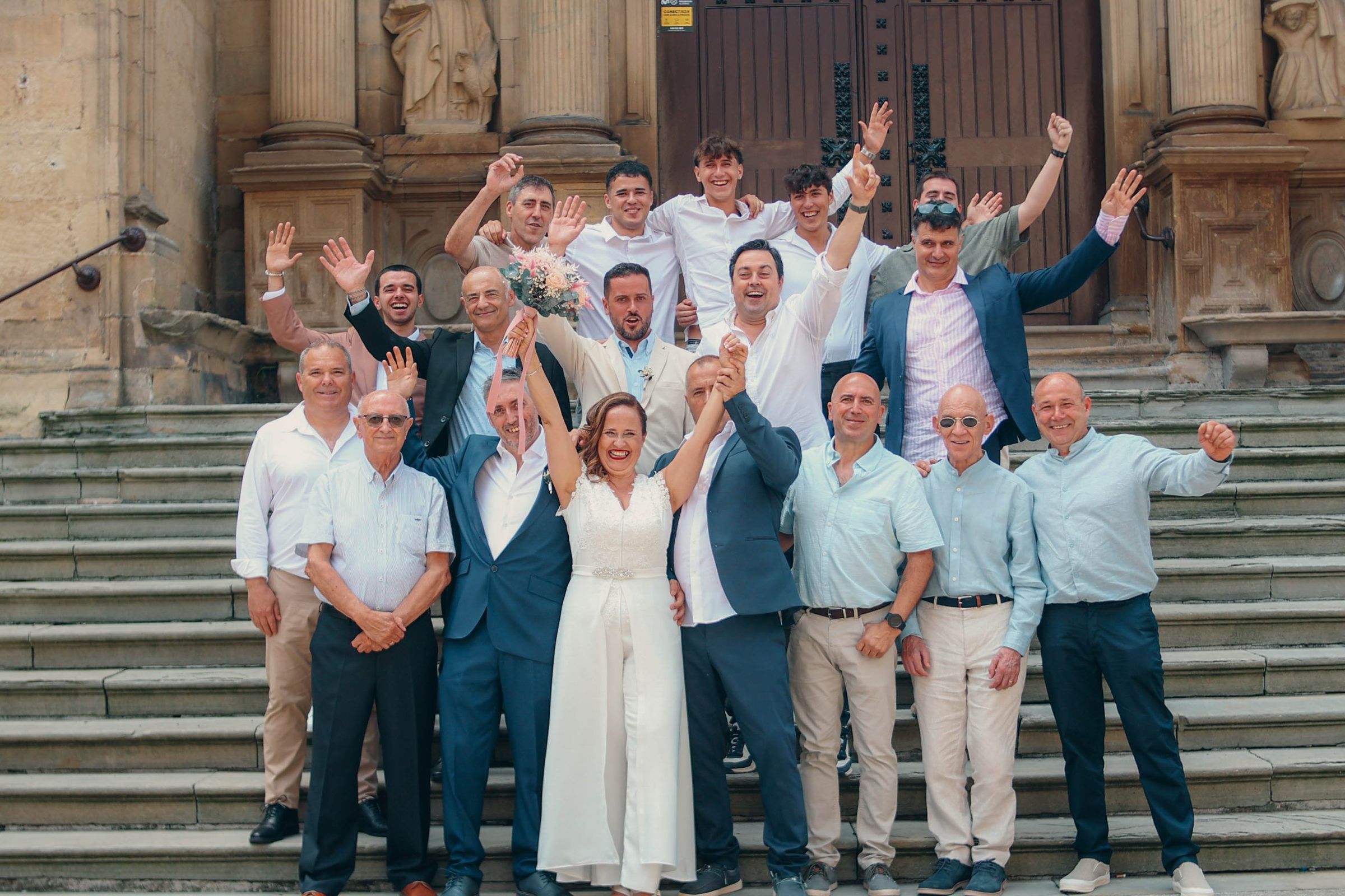 Novios celebrando con sus invitados en la escalinata, todos con los brazos en alto